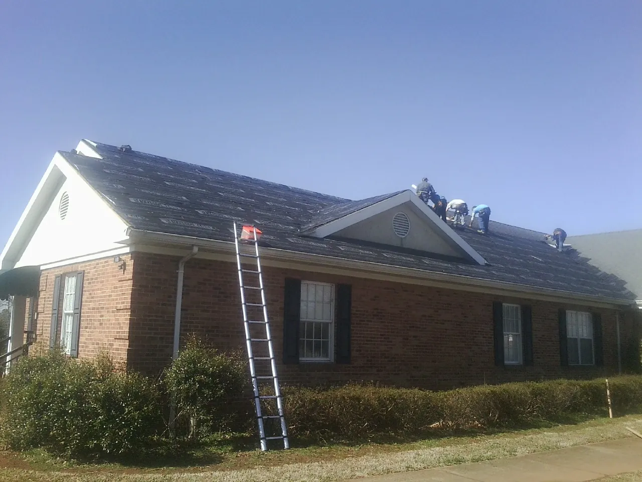 Crew tearing shingles off a brick ranch roof with a ladder set — Emergency Roof Repair work by our crew in Branford